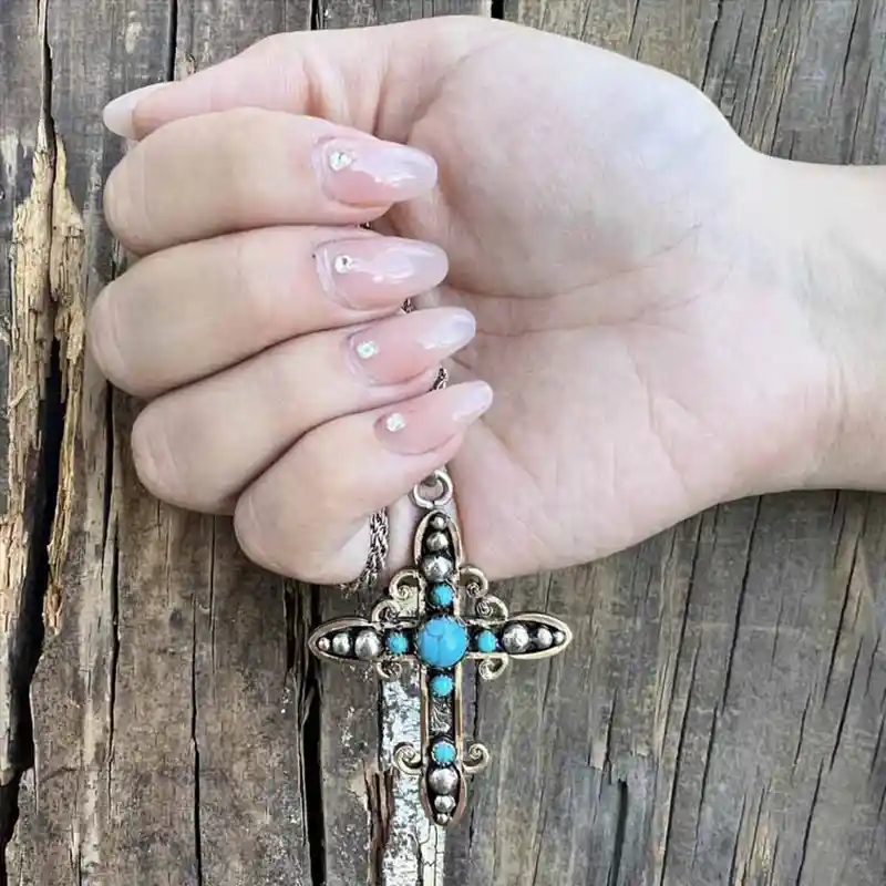 A turquoise cross pendant in a femenine hand